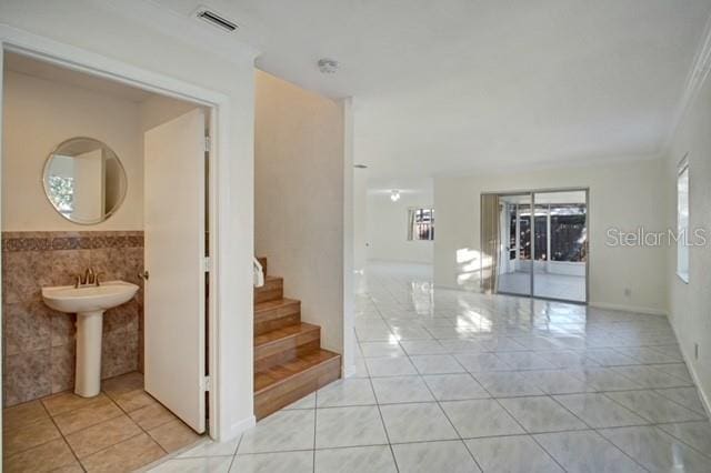 staircase with tile patterned floors, ornamental molding, and tile walls