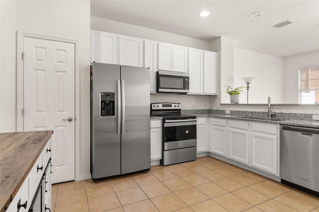 kitchen with sink, light tile patterned flooring, butcher block countertops, white cabinets, and appliances with stainless steel finishes