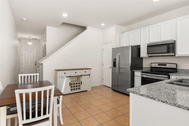 kitchen with light stone countertops, a textured ceiling, stainless steel appliances, light tile patterned floors, and white cabinetry