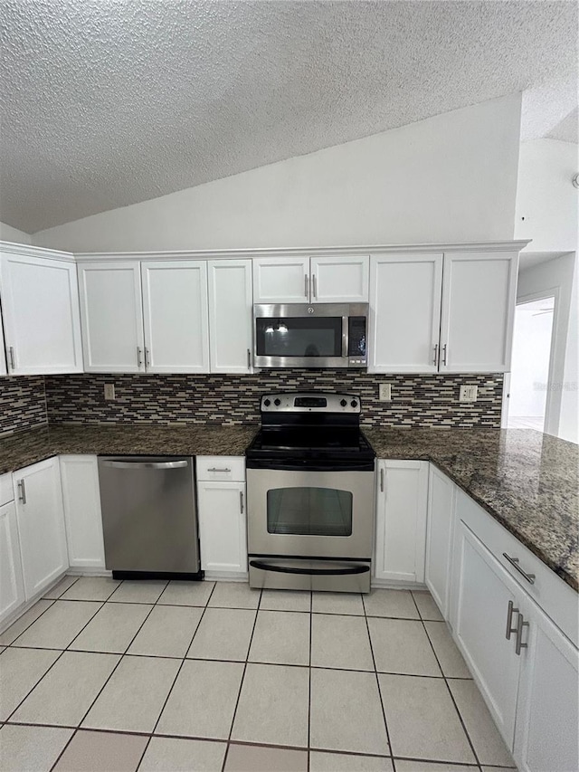 kitchen featuring appliances with stainless steel finishes, dark stone counters, white cabinetry, and lofted ceiling