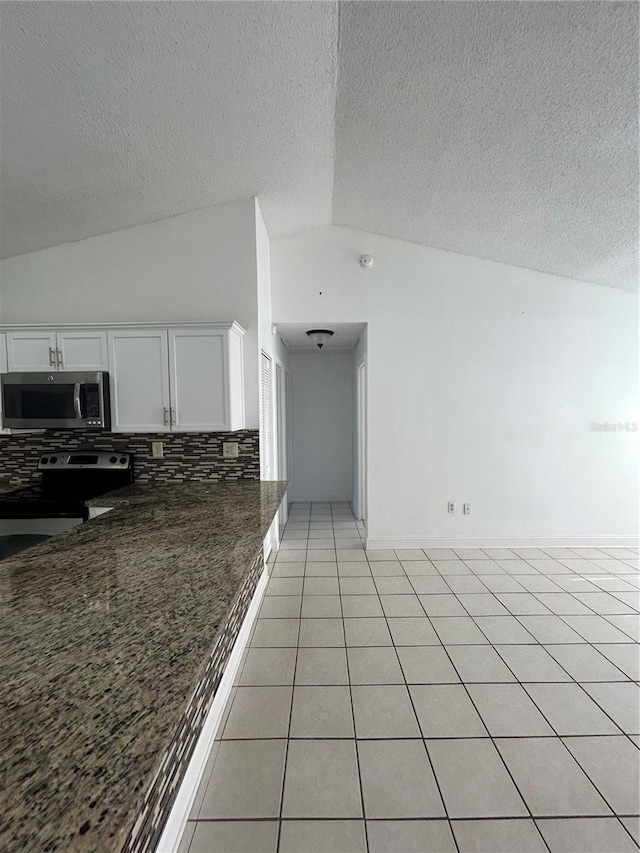 kitchen with lofted ceiling, dark stone counters, white cabinets, light tile patterned floors, and appliances with stainless steel finishes