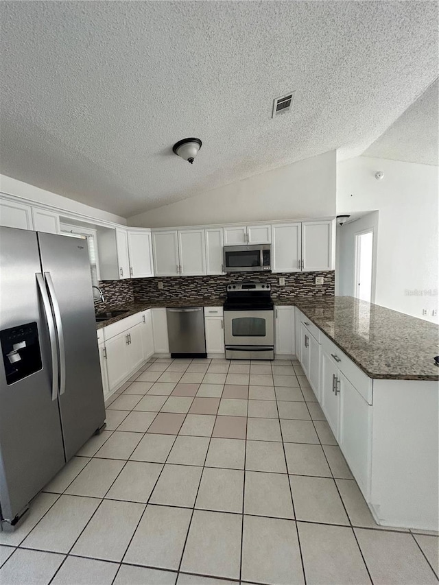 kitchen with kitchen peninsula, decorative backsplash, stainless steel appliances, vaulted ceiling, and white cabinetry