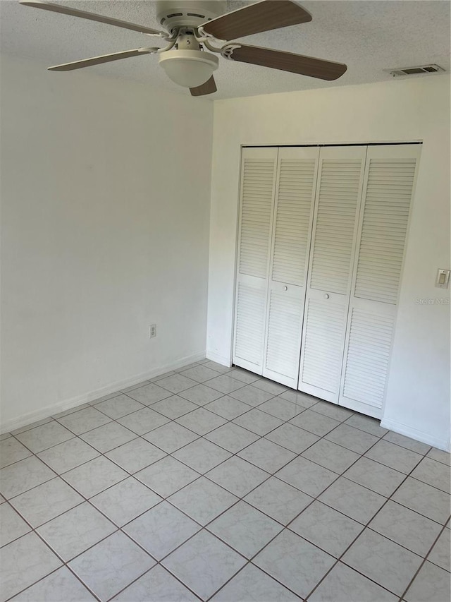 unfurnished bedroom featuring ceiling fan, a closet, light tile patterned flooring, and a textured ceiling