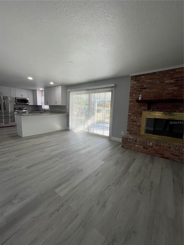 unfurnished living room featuring a brick fireplace, a textured ceiling, and light wood-type flooring