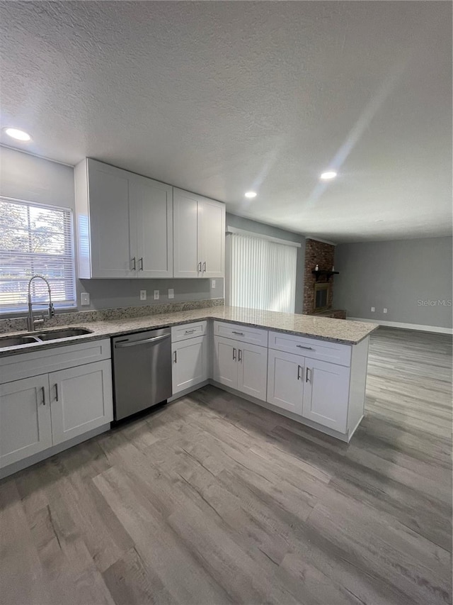 kitchen with dishwasher, white cabinets, sink, light wood-type flooring, and kitchen peninsula