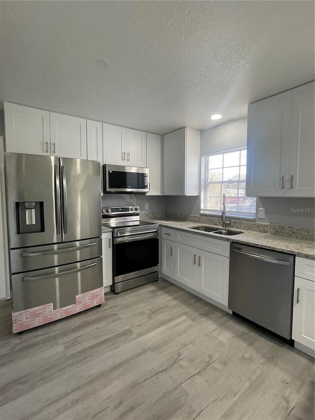 kitchen featuring appliances with stainless steel finishes, light hardwood / wood-style flooring, white cabinetry, and sink