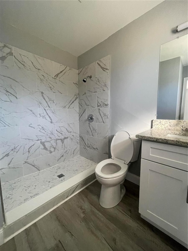 bathroom with tiled shower, hardwood / wood-style floors, vanity, and toilet