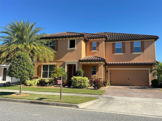 mediterranean / spanish-style home with a tile roof, an attached garage, decorative driveway, a front lawn, and stucco siding