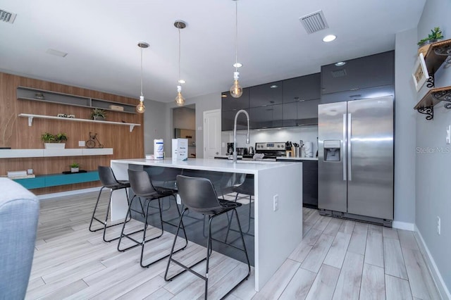 kitchen featuring light hardwood / wood-style flooring, decorative light fixtures, a breakfast bar area, a kitchen island with sink, and appliances with stainless steel finishes