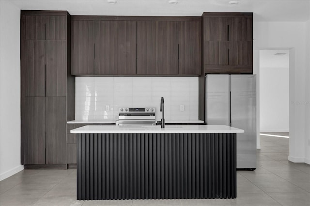 kitchen featuring dark brown cabinets, backsplash, stainless steel appliances, and a kitchen island with sink