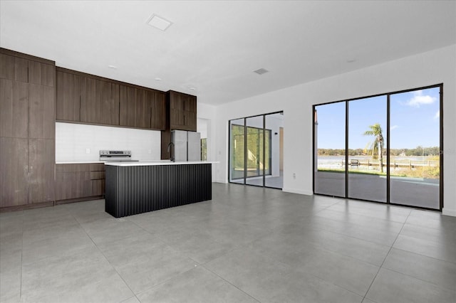 kitchen featuring white fridge, dark brown cabinetry, a kitchen island with sink, and electric stove