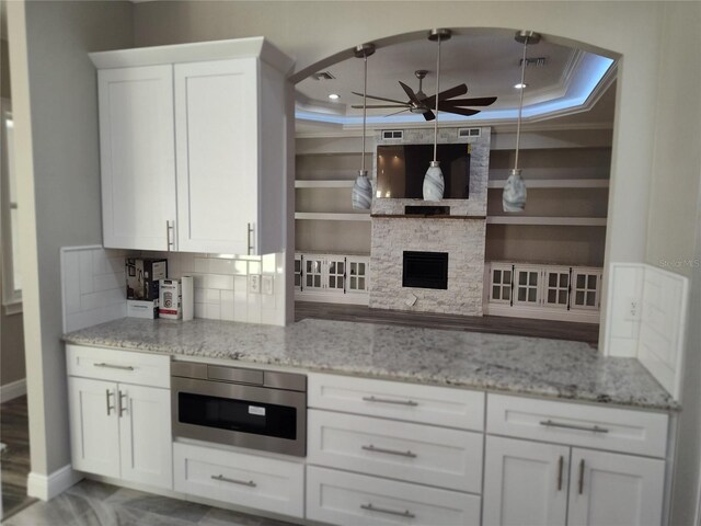 kitchen with a raised ceiling, a stone fireplace, stainless steel microwave, and white cabinets