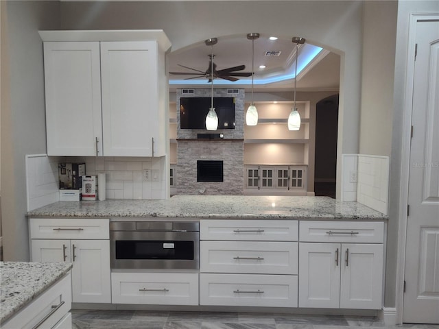 kitchen featuring white cabinets, pendant lighting, a raised ceiling, and light stone countertops