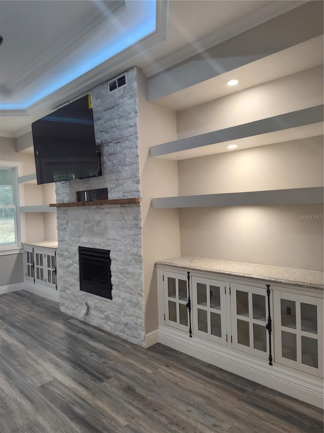 unfurnished living room with dark hardwood / wood-style floors, a stone fireplace, a tray ceiling, and crown molding