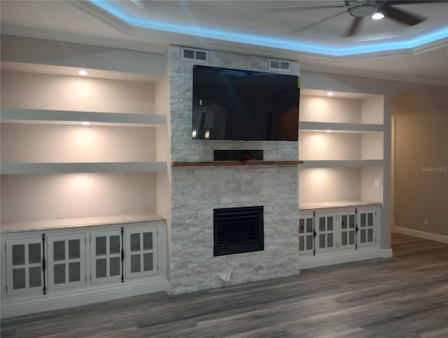 unfurnished living room featuring built in shelves, ceiling fan, a raised ceiling, and a stone fireplace