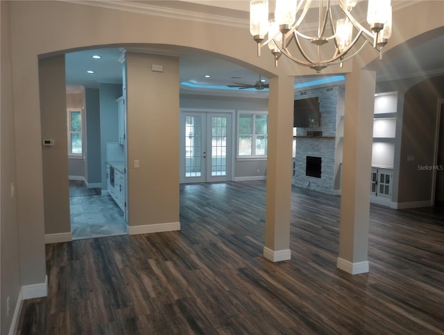 interior space featuring dark wood-type flooring, french doors, ceiling fan with notable chandelier, a stone fireplace, and crown molding