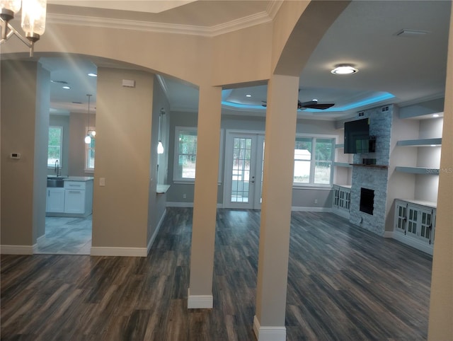 unfurnished living room featuring ornamental molding, a tray ceiling, ceiling fan, dark hardwood / wood-style floors, and a stone fireplace