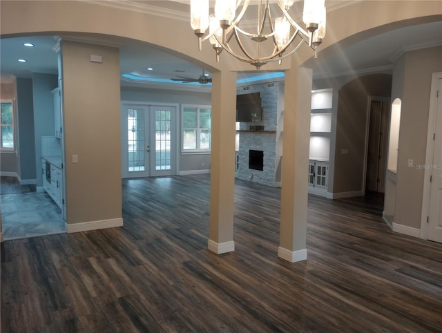 unfurnished living room featuring french doors, dark hardwood / wood-style floors, a fireplace, ceiling fan with notable chandelier, and ornamental molding