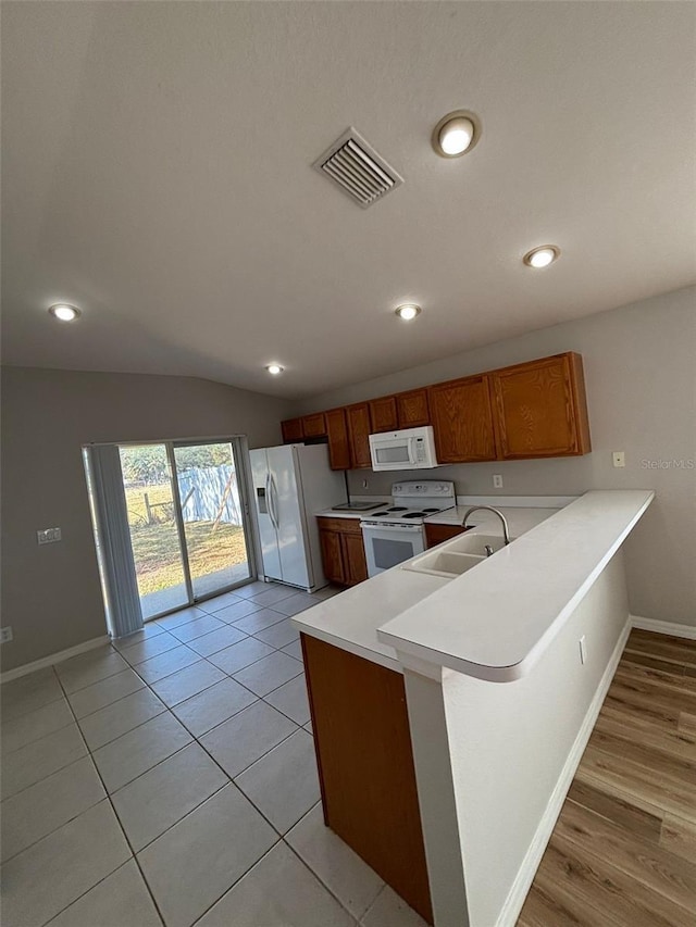 kitchen with kitchen peninsula, white appliances, vaulted ceiling, sink, and light tile patterned flooring