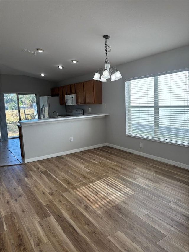 kitchen with hanging light fixtures, kitchen peninsula, hardwood / wood-style flooring, a notable chandelier, and stainless steel fridge with ice dispenser