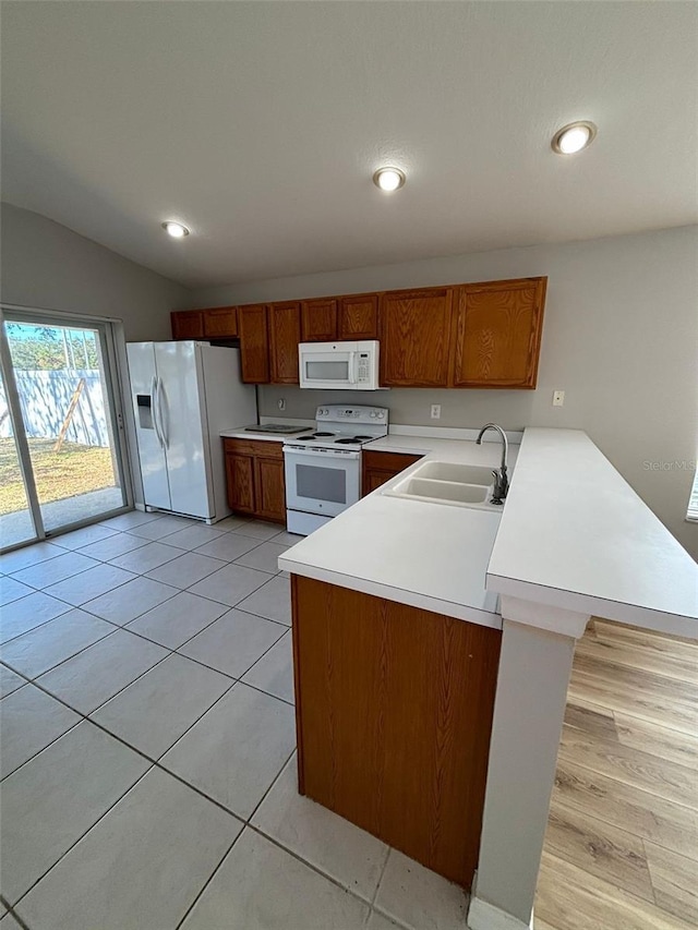 kitchen featuring sink, kitchen peninsula, vaulted ceiling, white appliances, and light tile patterned floors