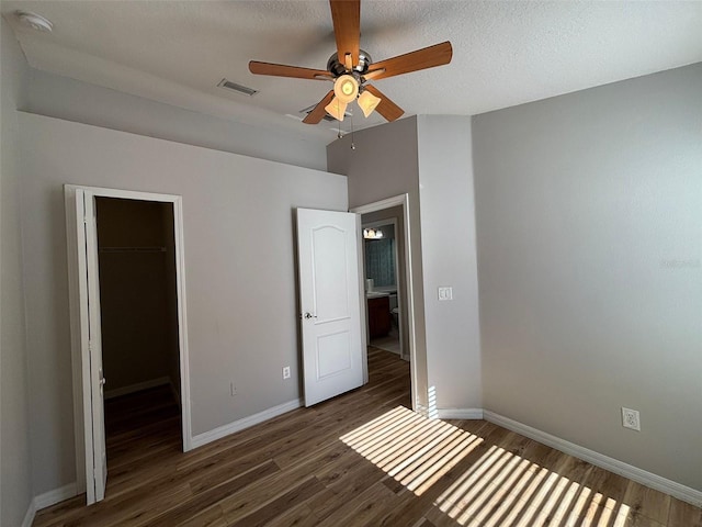 unfurnished bedroom featuring ceiling fan, dark hardwood / wood-style floors, a spacious closet, a textured ceiling, and a closet