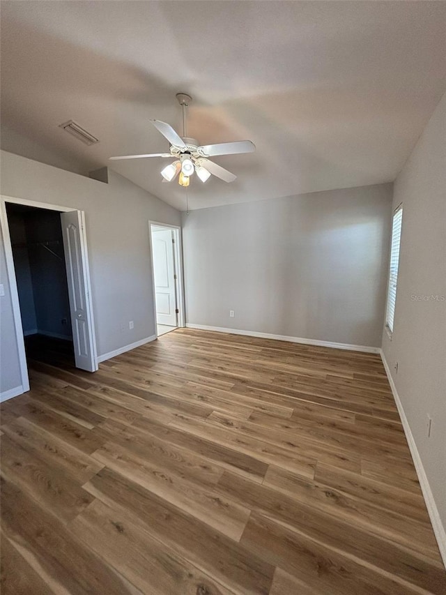 unfurnished bedroom featuring ceiling fan, dark hardwood / wood-style floors, a walk in closet, and a closet