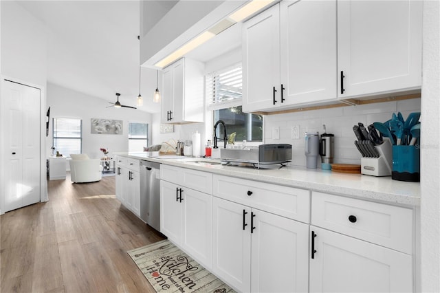 kitchen featuring tasteful backsplash, stainless steel dishwasher, light stone counters, vaulted ceiling, and white cabinets