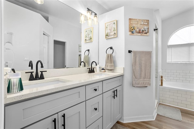 bathroom featuring vanity, wood-type flooring, and a relaxing tiled tub