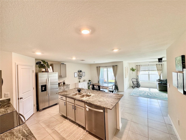 kitchen featuring light tile patterned flooring, an island with sink, sink, light stone counters, and stainless steel appliances