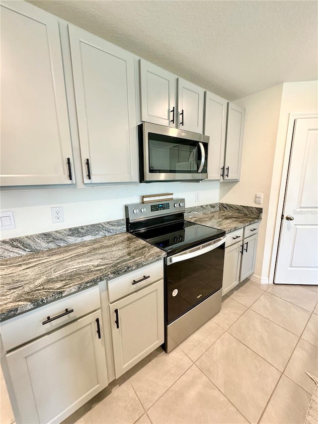 kitchen featuring a textured ceiling, light tile patterned floors, dark stone counters, stainless steel appliances, and white cabinets