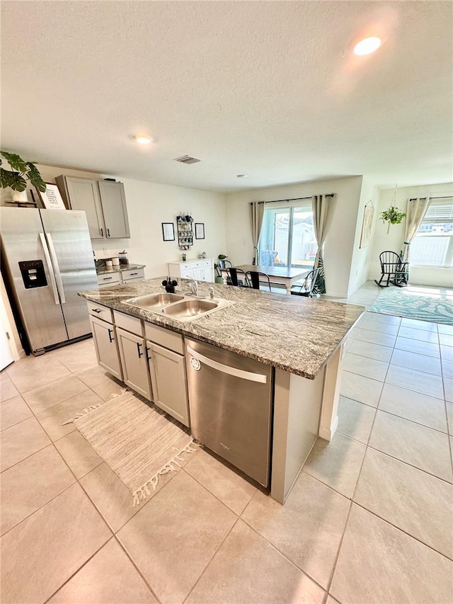 kitchen featuring light stone countertops, appliances with stainless steel finishes, sink, and a kitchen island with sink