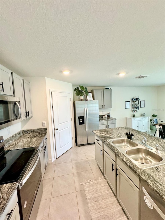 kitchen with sink, gray cabinetry, a textured ceiling, light tile patterned floors, and appliances with stainless steel finishes