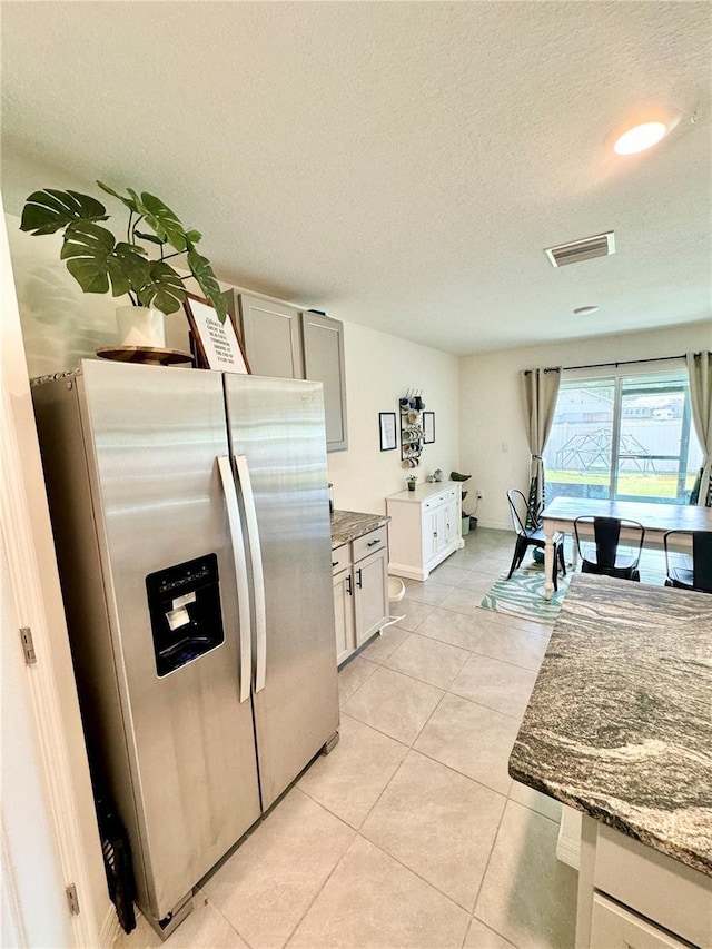 kitchen with stone counters, stainless steel refrigerator with ice dispenser, light tile patterned floors, and a textured ceiling