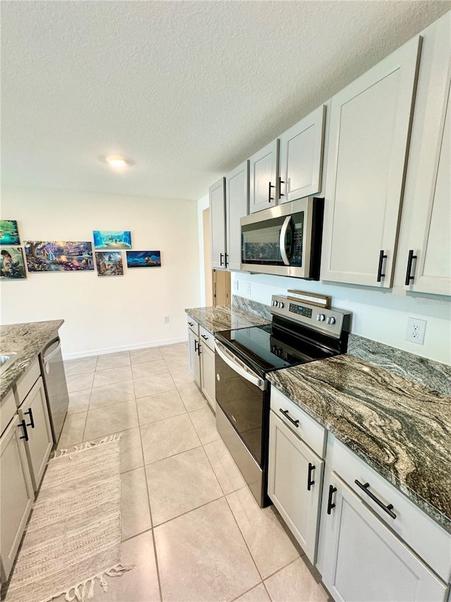 kitchen with a textured ceiling, light tile patterned floors, dark stone counters, stainless steel appliances, and white cabinets