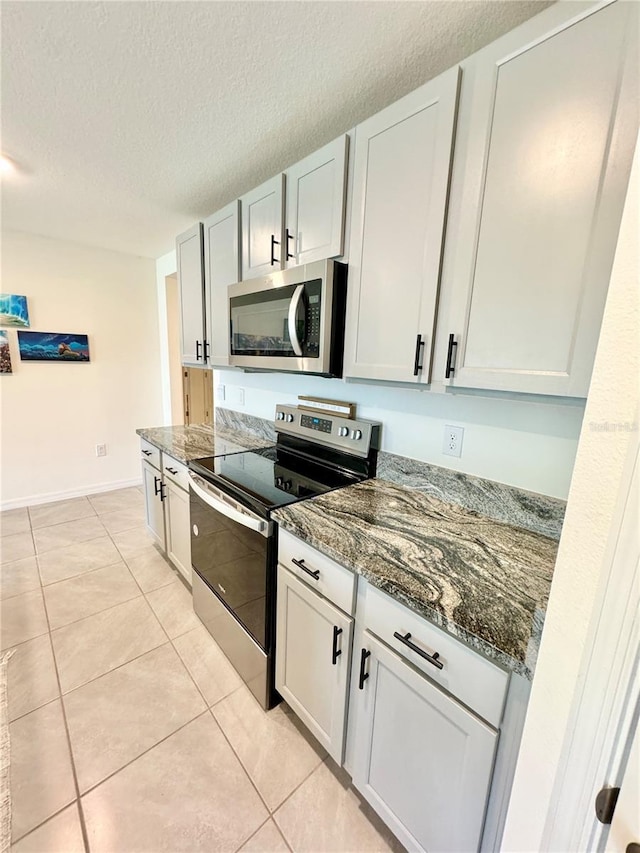 kitchen featuring dark stone countertops, stainless steel appliances, white cabinets, and light tile patterned flooring