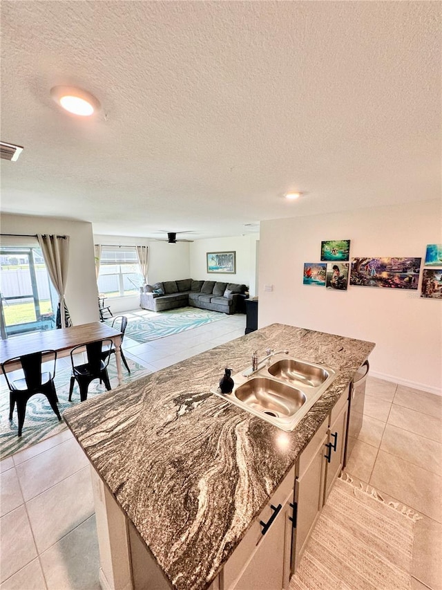 kitchen featuring sink, light stone counters, light tile patterned floors, dishwasher, and an island with sink