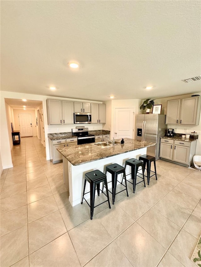 kitchen featuring sink, a breakfast bar, appliances with stainless steel finishes, a kitchen island with sink, and dark stone counters