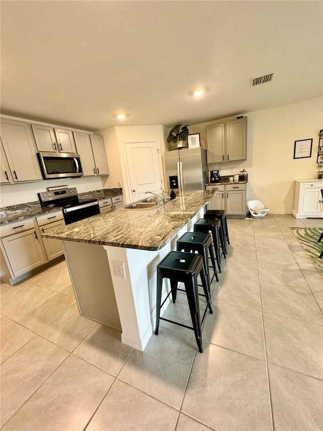 kitchen featuring sink, a breakfast bar area, a center island with sink, dark stone countertops, and appliances with stainless steel finishes