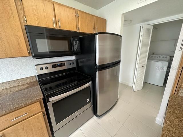 kitchen with appliances with stainless steel finishes, washer / clothes dryer, light tile patterned floors, and dark stone countertops