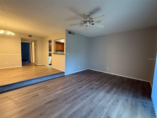 spare room with a textured ceiling, ceiling fan with notable chandelier, and dark wood-type flooring