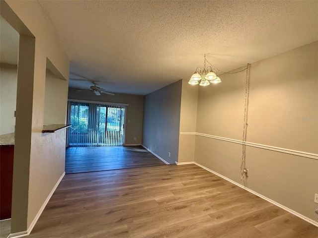 spare room with a textured ceiling, wood-type flooring, and ceiling fan with notable chandelier