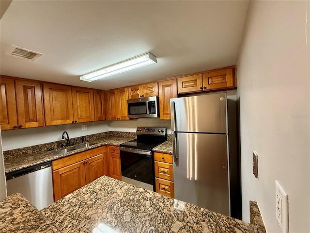 kitchen featuring appliances with stainless steel finishes, dark stone counters, and sink