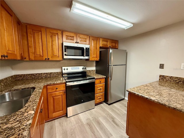 kitchen with light wood-type flooring, stainless steel appliances, dark stone counters, and sink