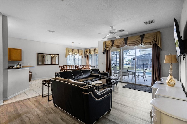 living room featuring ceiling fan with notable chandelier, a textured ceiling, light hardwood / wood-style flooring, and plenty of natural light