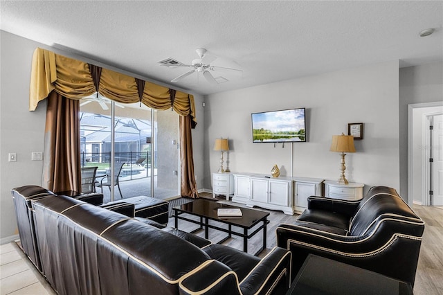 living room featuring ceiling fan, light hardwood / wood-style floors, and a textured ceiling