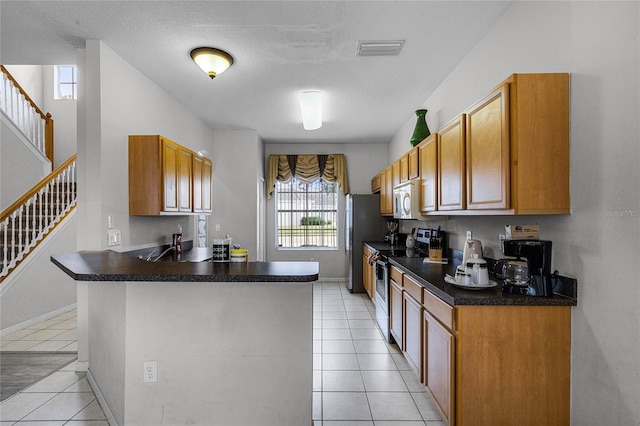 kitchen with kitchen peninsula, light tile patterned flooring, stainless steel appliances, and a textured ceiling