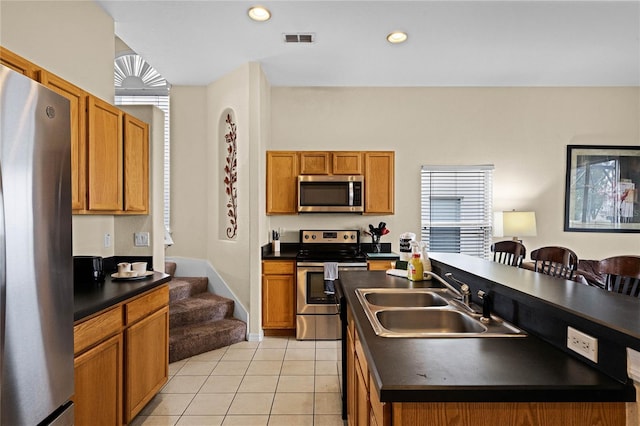 kitchen featuring appliances with stainless steel finishes, light tile patterned floors, a kitchen island with sink, and sink