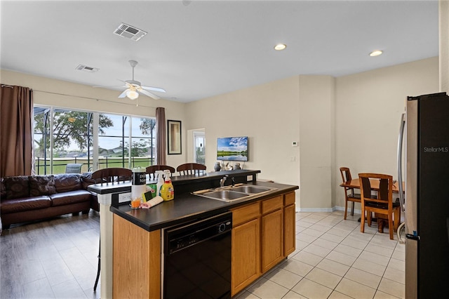 kitchen featuring ceiling fan, sink, a center island with sink, black dishwasher, and stainless steel refrigerator