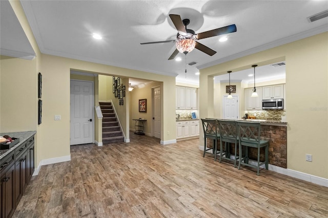 kitchen with a kitchen breakfast bar, backsplash, ornamental molding, light hardwood / wood-style flooring, and white cabinets